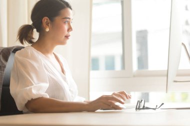 Ofiste bilgisayar kullanan gülümseyen Asyalı genç iş kadını..