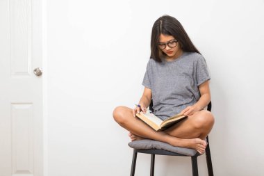 Happy young Asian woman reading on chair in the living room at home