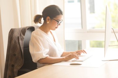 Ofiste bilgisayar kullanan gülümseyen Asyalı genç iş kadını..