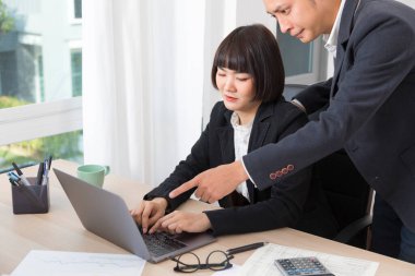 Asyalı işadamı ya da patron gülümseyip bilgisayarı işaret ederken kadın çalışan ve daktilo yazan.