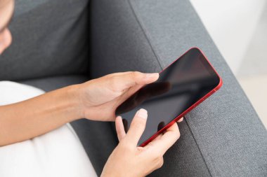 Kanepede oturan ve bir akıllı telefon kullanan kadın