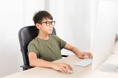 Cute Asian boy with eyeglasses study online via computer on table at home.