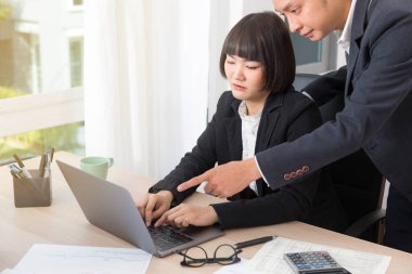 Asyalı işadamı ya da patron gülümseyip bilgisayarı işaret ederken kadın çalışan ve daktilo yazan.