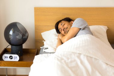 Yatak odasındaki yatakta uyuyan yakışıklı Asyalı adam, battaniyeyle örtülü..