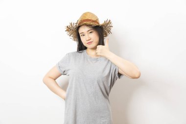 Beyaz arka planda duran gri tişörtlü ve hasır şapkalı Asyalı kız..