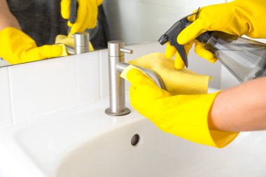 Sarı eldivenli eller banyoda lavaboyu temizliyor. Banyo dezenfekte ediliyor. Koronavirüs enfeksiyonunun önlenmesi