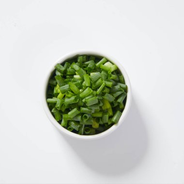 Dilimlenmiş taze soğanlar beyaz arka planda bir fincanda.