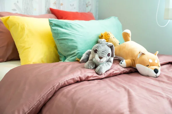 Yatağın üzerinde renkli yastıklar ve oyuncak bebekler var.
