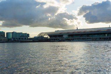 Amsterdam, Hollanda - 29 Kasım 2019: Centraal Demiryolu İstasyonu Terminal Salonu 29 Kasım 2019 'da Hollanda' nın Amsterdam kentinde mavi gökyüzü altında beyaz bulutlarla IJ suyundan görüldü..