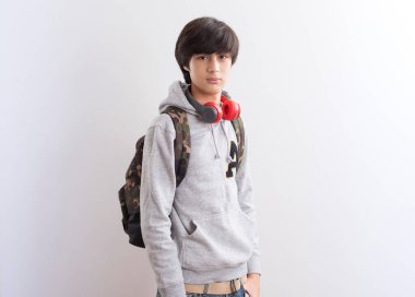 Beyaz arka planda sırt çantası ve kulaklığı olan genç bir çocuk.