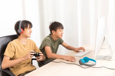 Kulaklıklı iki genç çocuk evde oyun oynamak için bilgisayar kullanıyor. Mutlu Asyalı çocuk evde online oyun oynuyor..