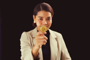 Successful Asian businesswoman standing over black background holding bitcoin money.