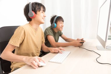 Kulaklıklı iki genç çocuk evde oyun oynamak için bilgisayar kullanıyor. Mutlu Asyalı çocuk evde online oyun oynuyor..