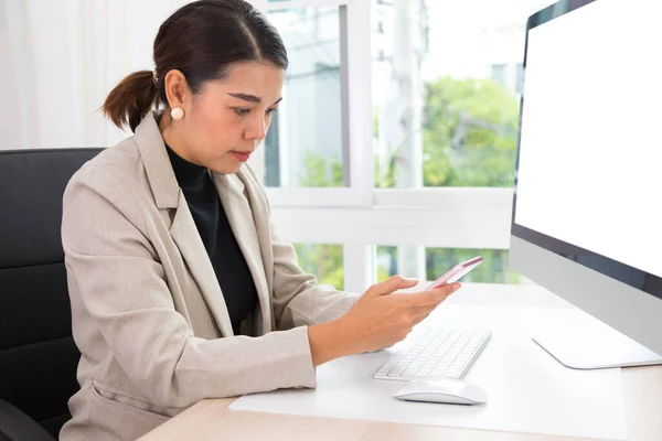 アジアの女性起業家は彼女のオフィスでの仕事で忙しい 机の上でコンピューターを操作しながらスマートフォンや携帯電話で話す若いアジアの女性 — ストック写真