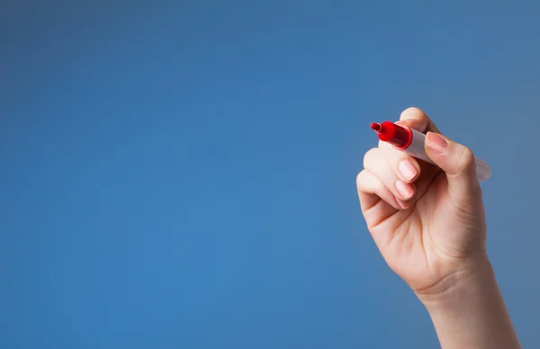 Vrouwelijke hand met zwarte whiteboard marker op een blauwe achtergrond — Stockfoto