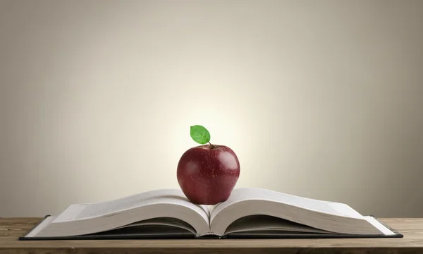Aufgeschlagenes Buch auf einem Holztisch mit rotem Apfel — Stockfoto