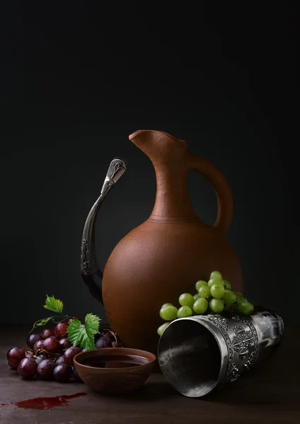 Cup of wine pitcher drinking horn and grapes on a wooden table — Stock Photo, Image
