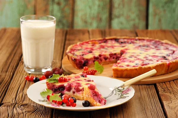 Gooseberry pie slice on white plate, glass of milk and pie on round bamboo serving board