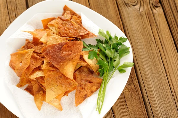 Fried spicy lavash chips in white plate with fresh parsley