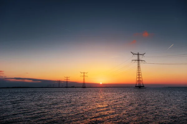 Elektrische lijn boven water tijdens een fantastische zonsondergang. — Stockfoto