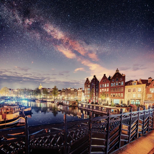 Beautiful night in Amsterdam. Night illumination of buildings and boats near the water in the canal.