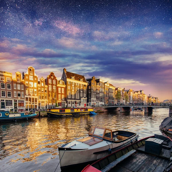 Beautiful night in Amsterdam. Night illumination of buildings and boats near the water in the canal.