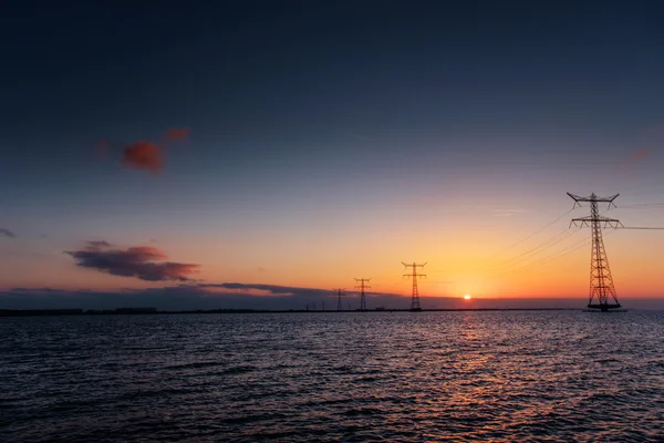 Elektrische lijn boven water tijdens een fantastische zonsondergang. — Stockfoto