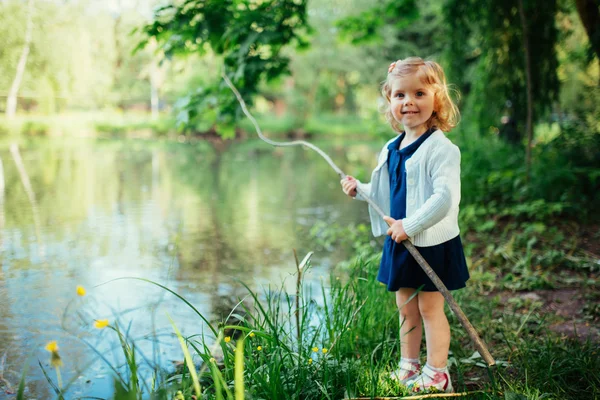 Schattig klein blonde meisje is tegen de achtergrond van water en g — Stockfoto