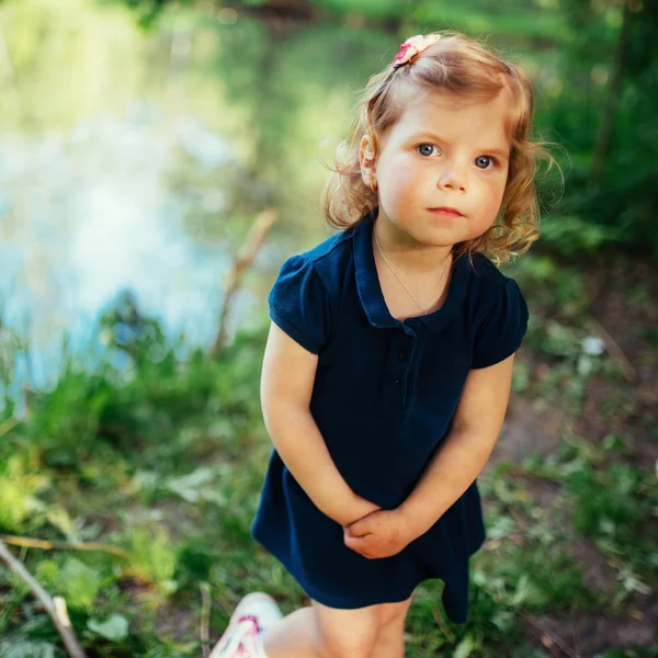 Schattig klein blonde meisje is tegen de achtergrond van water en g — Stockfoto