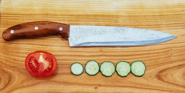 Деревянная доска с ножом, помидорами и огурцом — стоковое фото