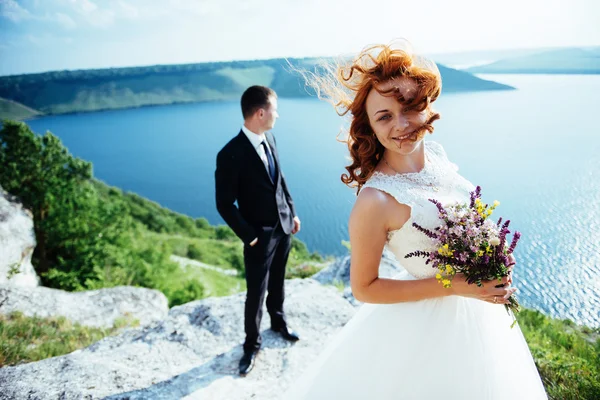 Gorgeous blonde bride and groom classy on the rocks, amid the se — Stock Photo, Image