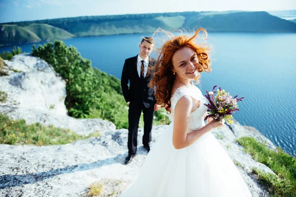 Hermosa novia rubia y novio con clase en las rocas, en medio de la se — Foto de Stock