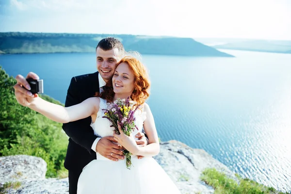 Gorgeous blonde bride and groom classy on the rocks, amid the se — Stock Photo, Image