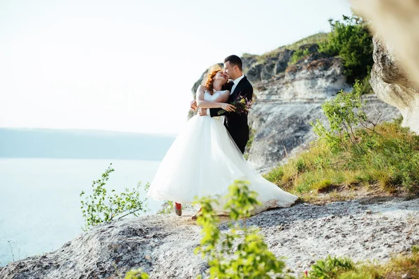 Splendida bionda sposa e sposo di classe sulle rocce, in mezzo al se — Foto Stock