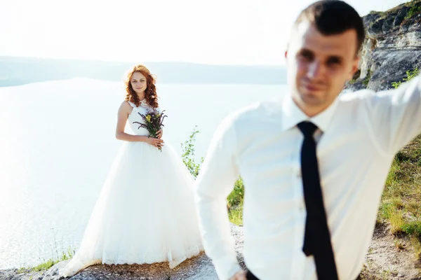Linda noiva loira e noivo elegante nas rochas, em meio ao se — Fotografia de Stock