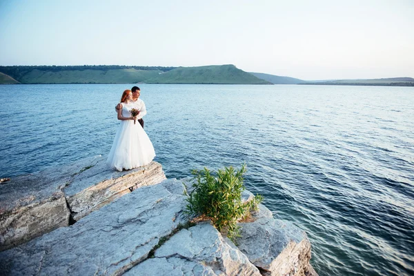 Πανέμορφη ξανθιά νύφη και κομψό γαμπρό σε βράχια, σε t — Φωτογραφία Αρχείου