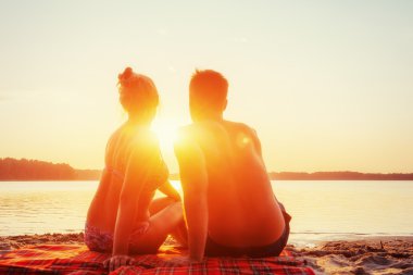 Sahilde romantik bir çift. Arka planda renkli bir günbatımı.