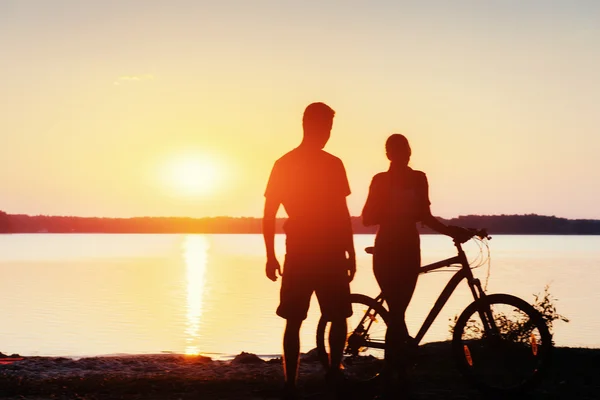 Koppel op een fiets bij zonsondergang aan het meer — Stockfoto