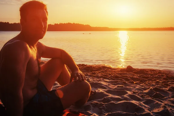 Homem sentado na areia ao pôr do sol — Fotografia de Stock