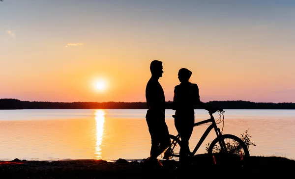 Para na rowerze na zachód słońca nad jeziorem — Zdjęcie stockowe