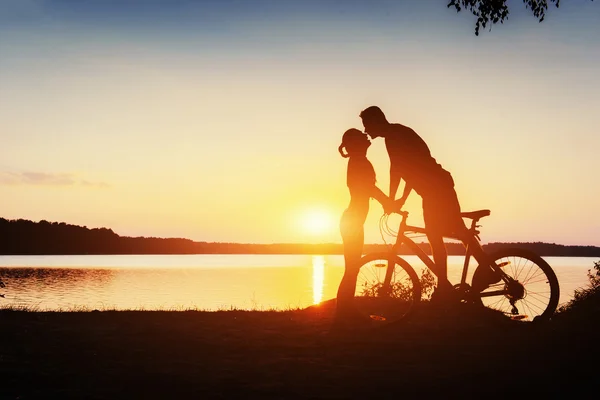 Koppel op een fiets bij zonsondergang aan het meer — Stockfoto