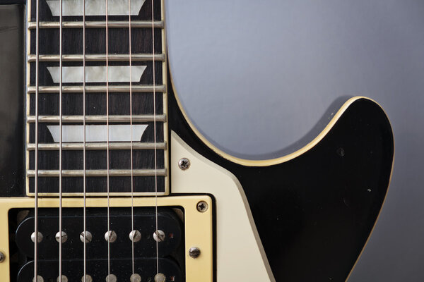 An electric guitar's neck in front of grey wall
