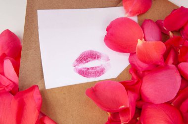 Zarfın içinde pembe gül yaprakları ve beyaz arka planda izole edilmiş öpücük ruju.