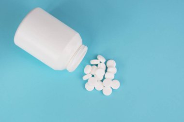 Beyaz yuvarlak haplar ve mavi arka planda şişe.