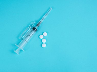 Mavi arka planda şırınga, ampul ve beyaz haplar.