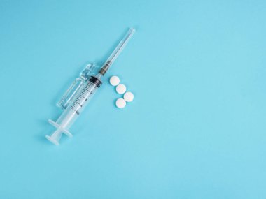 Mavi arka planda şırınga, ampul ve beyaz haplar.