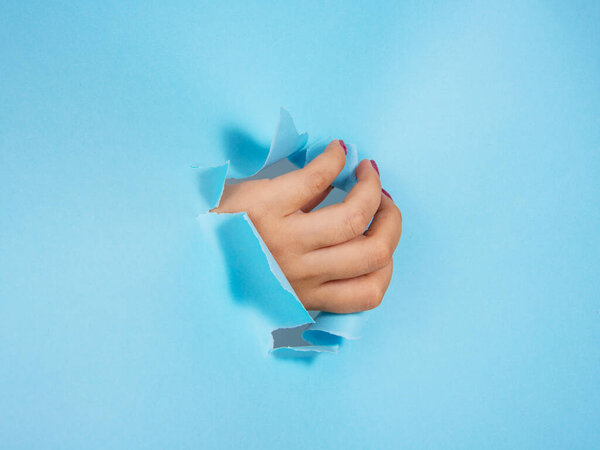 Woman hand in whole of torn blue paper background