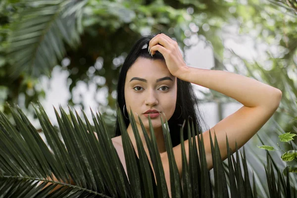 Retrato de beleza de mulher. Sexy atraente modelo asiático com maquiagem nua e penteado de rabo de cavalo, tocando a cabeça e olhando para a câmera, posando contra plantas tropicais. Beleza natural — Fotografia de Stock