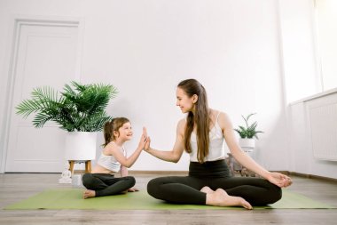 Anne ve küçük kızı yoga yapıyor evde ya da spor salonunda egzersiz yapıyor, Lotus pozunda birlikte oturuyorlar. Sağlıklı bir yaşam tarzı. Aile yogası