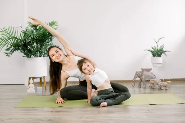 Balanced life, healthy lifestyle, family concept. Pretty Caucasian mother woman with little cute daughter, doing yoga relaxation and stretching exercise at home — Stock Photo, Image